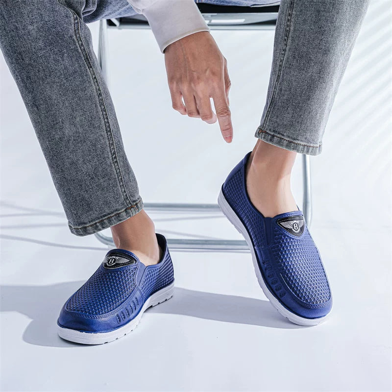 Siniset slip-on loaferit valkoisella pohjalla jalassa farkkujen kanssa istuma-asennossa — Helvenza