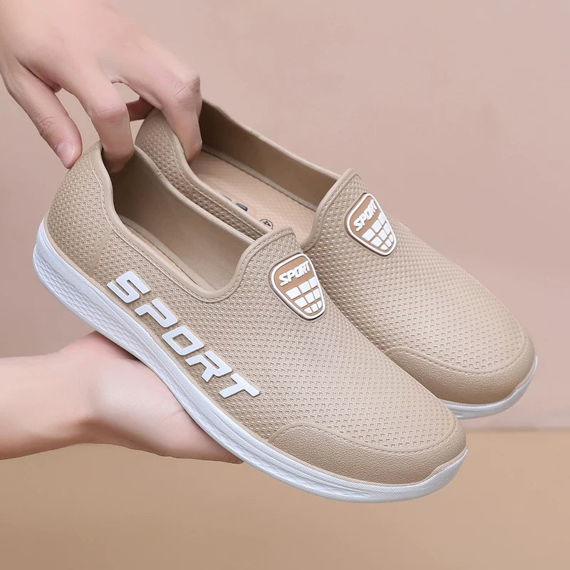Beige slip-on lenkkarit sport-logolla käsissä edestä — Helvenza