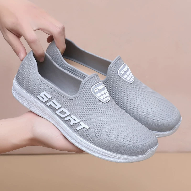Harmaat slip-on lenkkarit sport-logolla käsissä edestä — Helvenza
